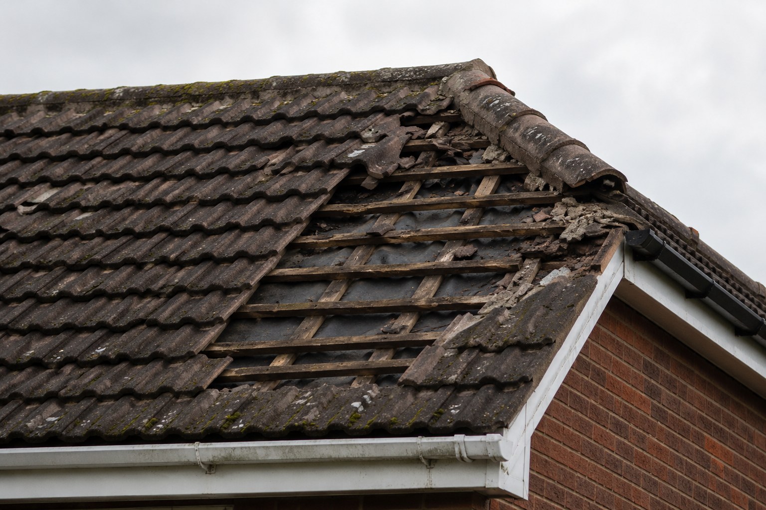 A residential roof with a section of missing and broken tiles exposing the timber battens